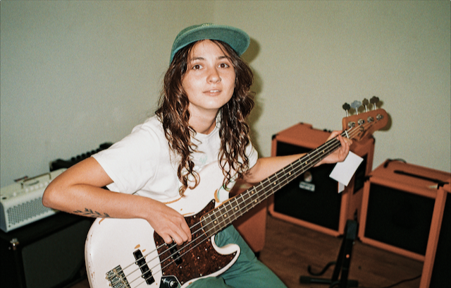 Junge Frau mit grüner Kappe spielt Gitarre und schaut dabei in die Kamera..