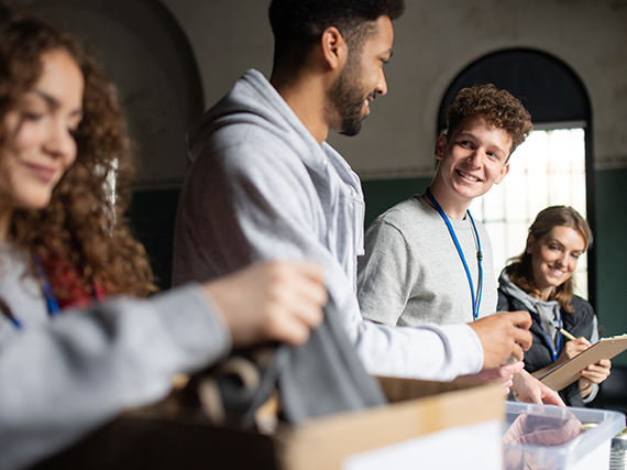 Vier freiwillige Personen stehen vor einem Tisch und legen Kleidung in Kartons.