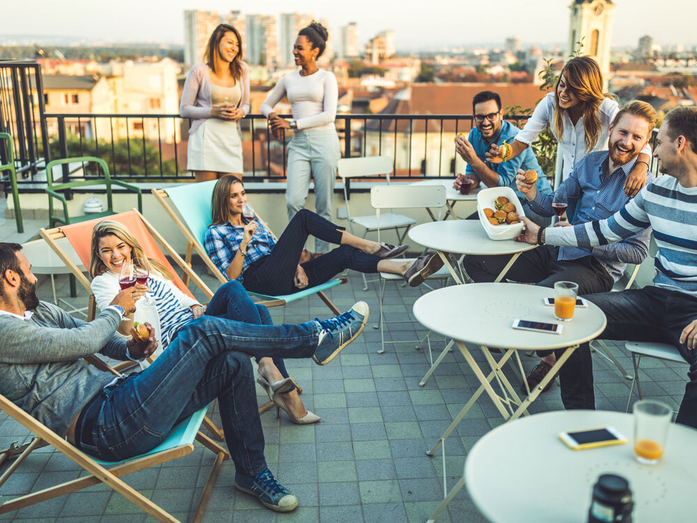 Personen sitzen auf einer Dachterasse mit Getränken und essen Burger.