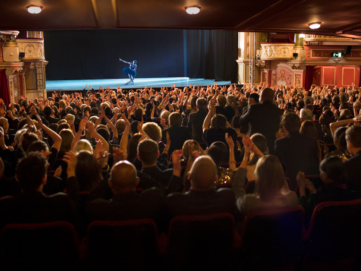Ein Tänzer auf der Bühne verbeugt sich vor einem applaudierenden Publikum in einem prunkvollen Theater.