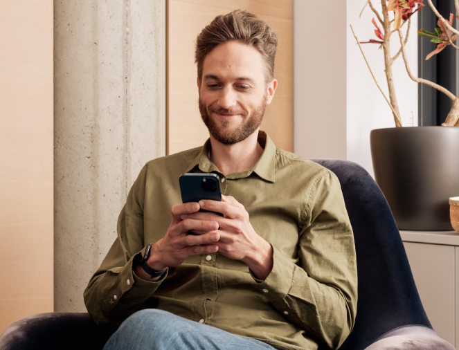 Ein Mann sitzt in einem Sessel und hält sein Handy in der Hand.