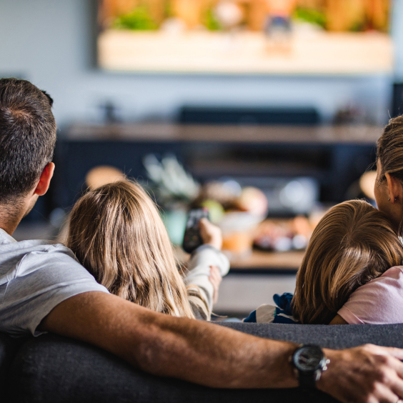 Familie schaut auf dem Sofa zusammen fernsehen.