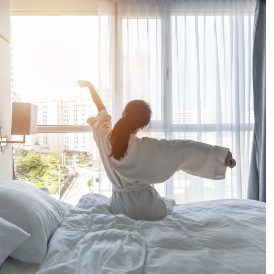 Frau sitzt auf dem Bett im Hotel und streckt sich.