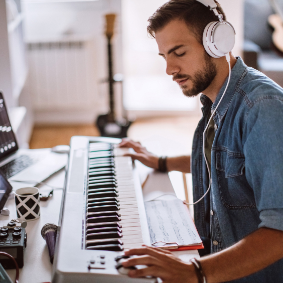 Mann sitzt mit Kopfhörern am Keyboard.