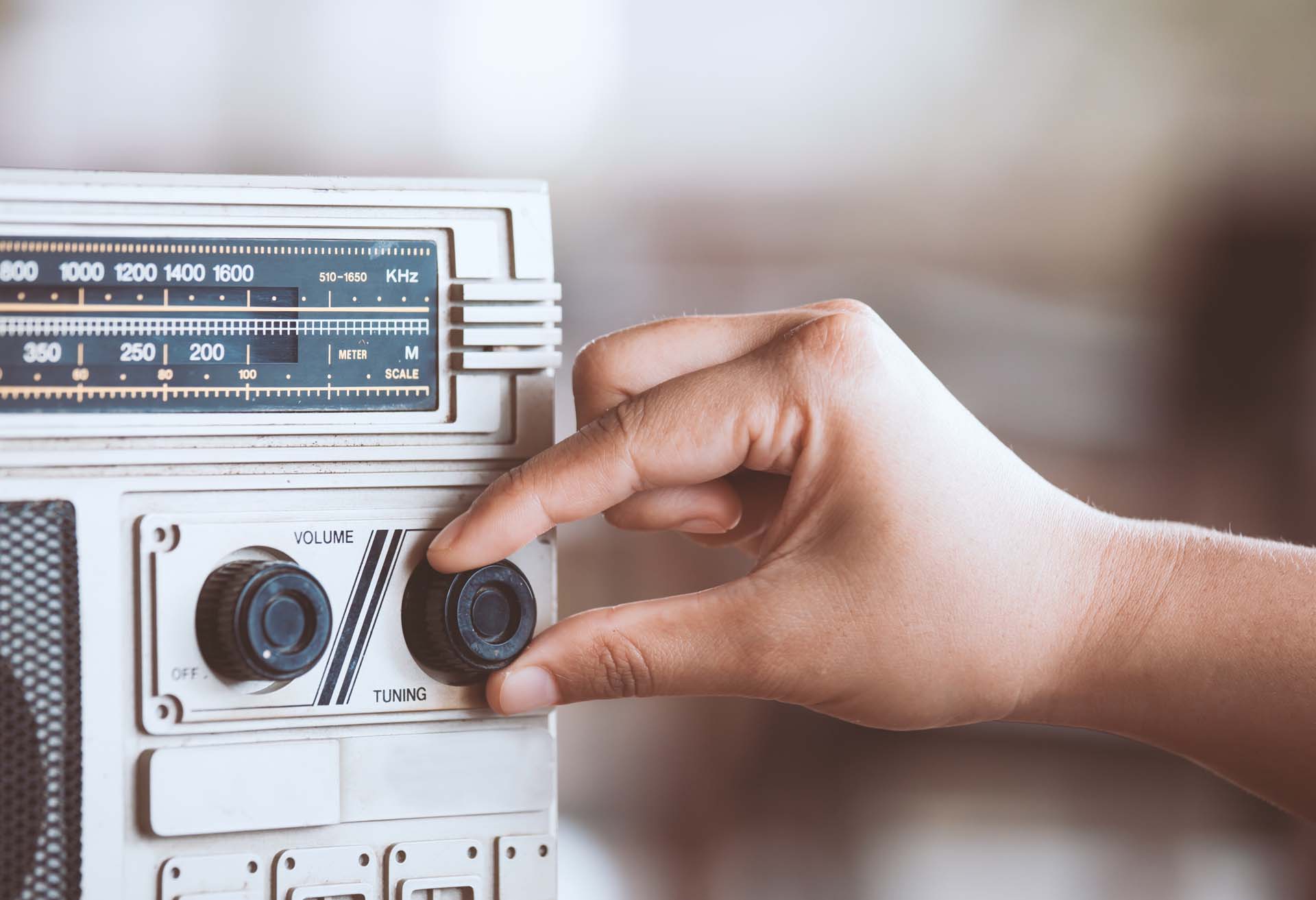Hand adjusting the tuning knob on a vintage radio with a visible frequency scale.
