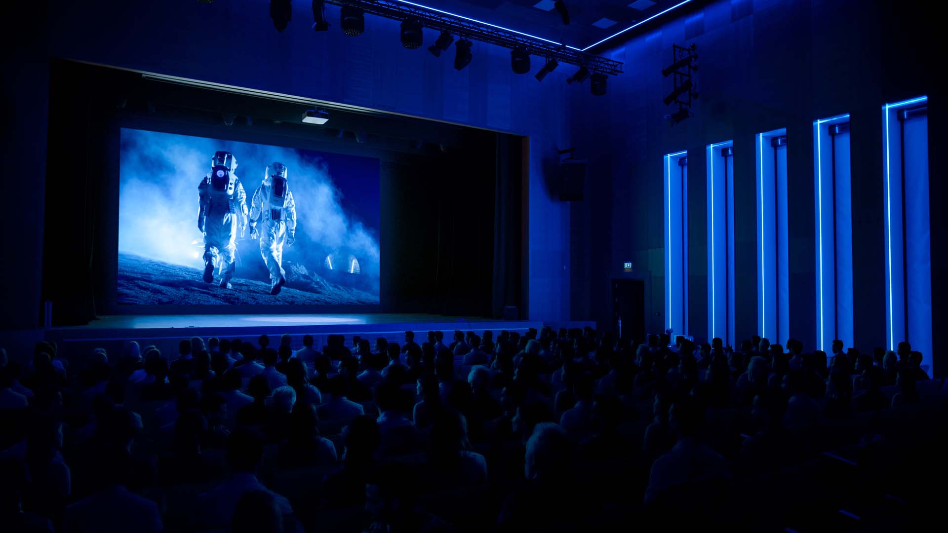 Gefüllter Kinosaal mit Astronauten auf der Leinwand