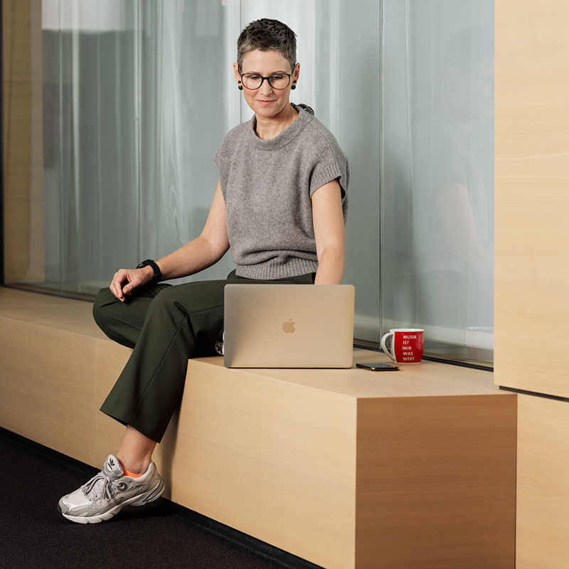 Frau sitzt auf einer Holzbank und arbeitet am Laptop.