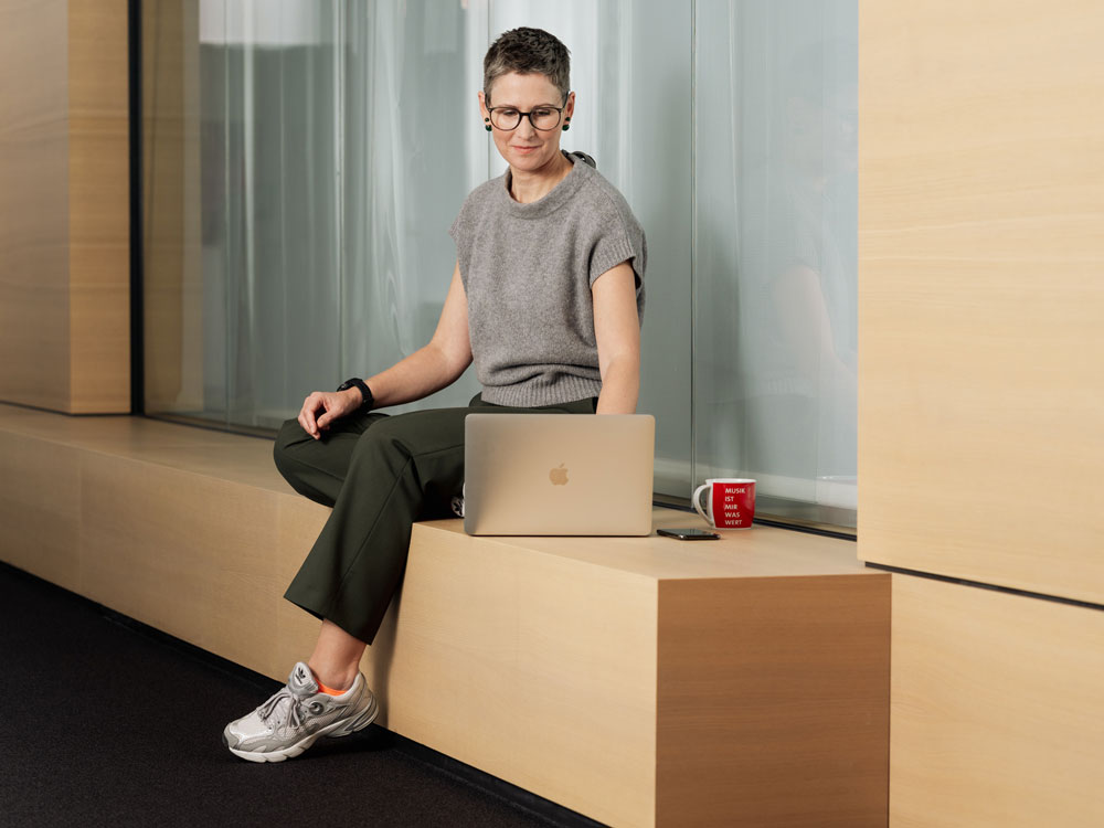 Frau sitzt auf einer Holzbank und arbeitet am Laptop.