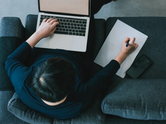 Mann auf Couch mit Laptop und Notizblatt