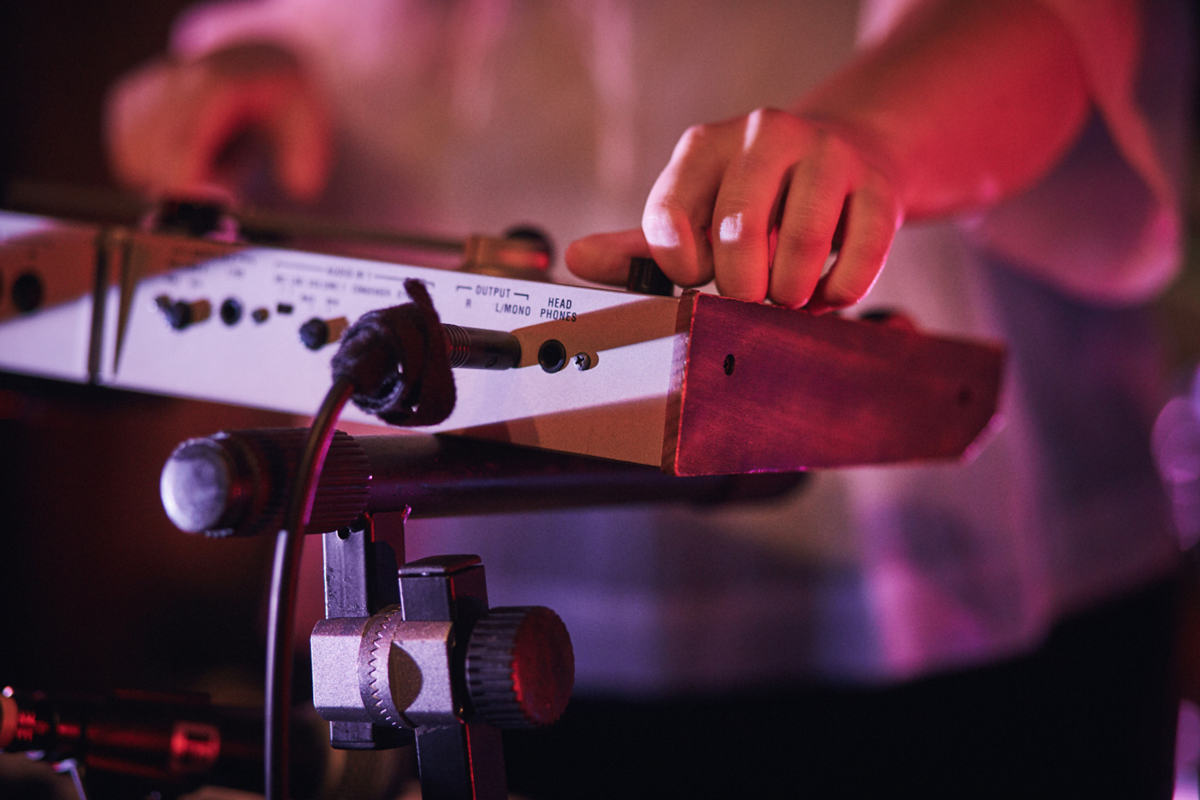 Hände bedienen ein elektronisches Musikinstrument auf einem Stativ, beleuchtet von pinkem Licht.