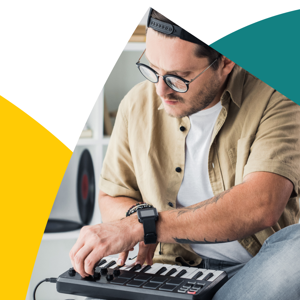 Man with glasses and cap using a MIDI keyboard, surrounded by colorful abstract shapes.