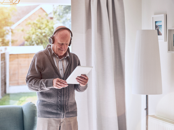 Älterer Mann hört mit Kopfhörern Musik und hält sein Tablet in der Hand.