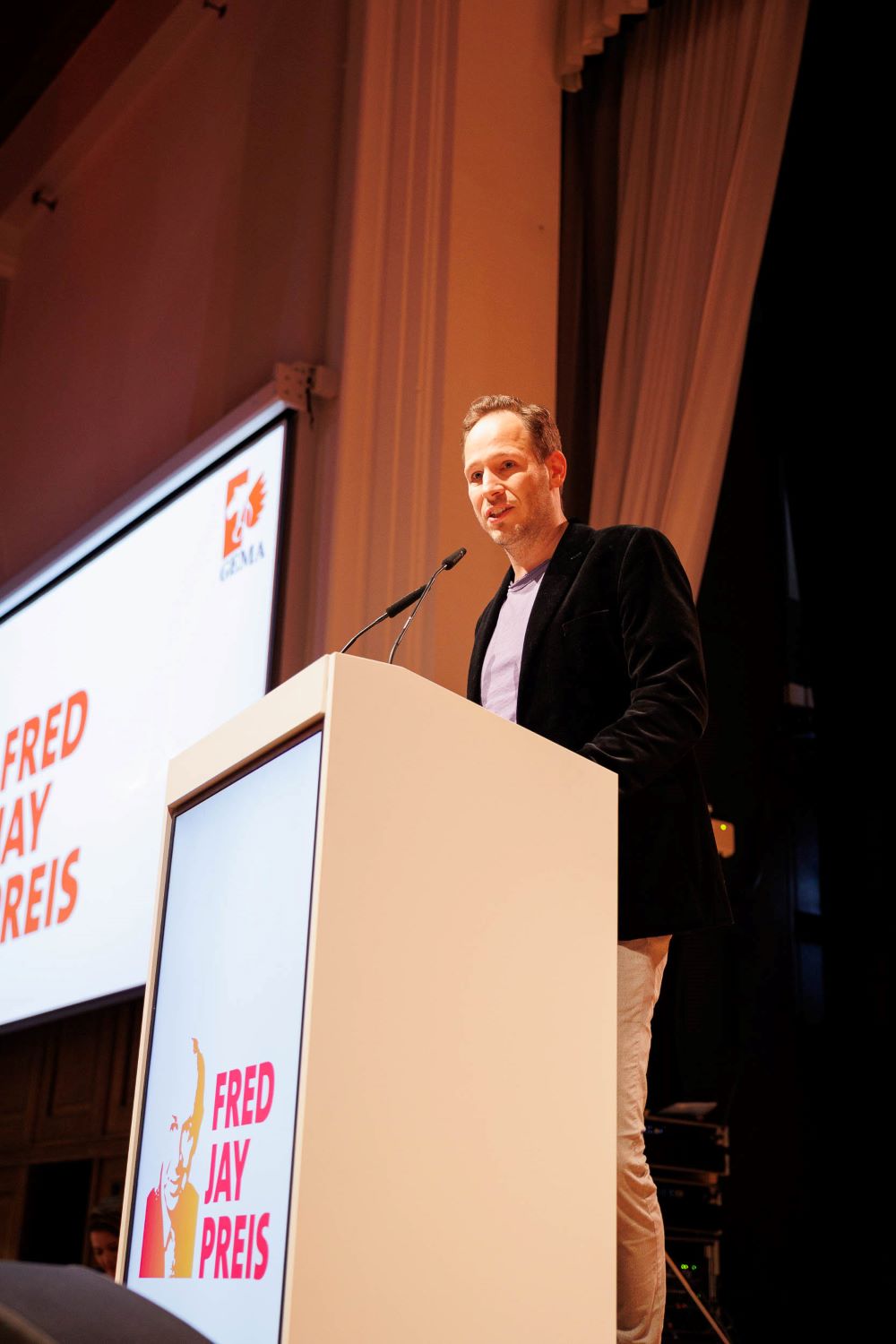 Jurysprecher Tobias Reitz hinter einem Rednerpult mit Flasche in der Hand