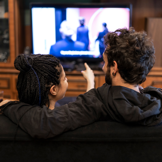 Eine Frau und ein Mann sitzen gemeinsam auf der Couch und schauen TV.