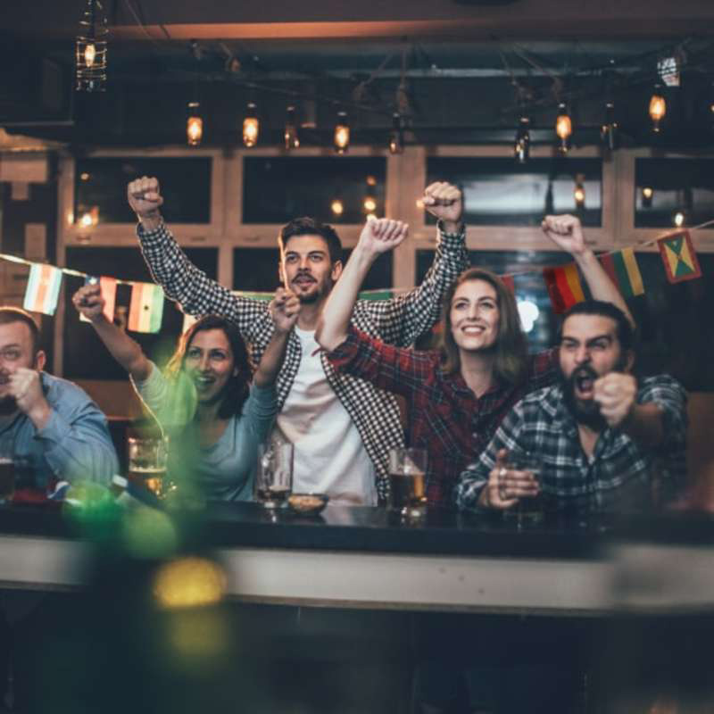 Mehrere Personen jubeln in einer Sportsbar.