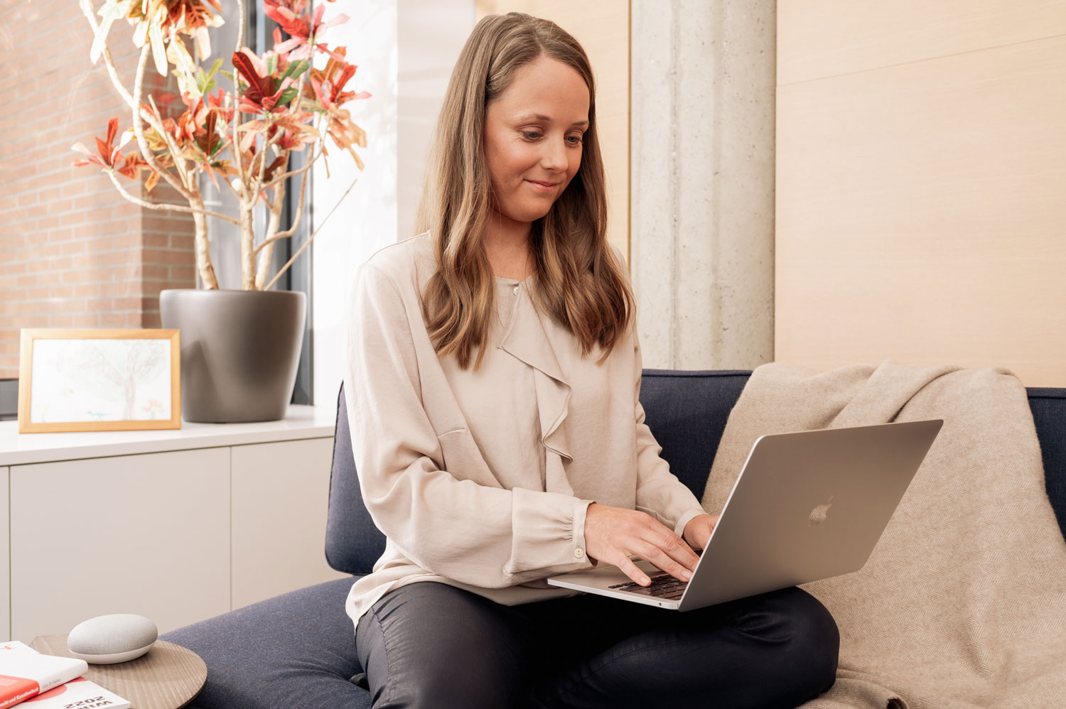 Junge Frau sitzt auf einem Sofa und arbeitet an ihrem Laptop