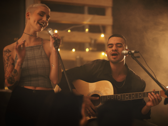 Zwei Personen singen gemeinsam auf einer Bühne, einer spielt Gitarre.
